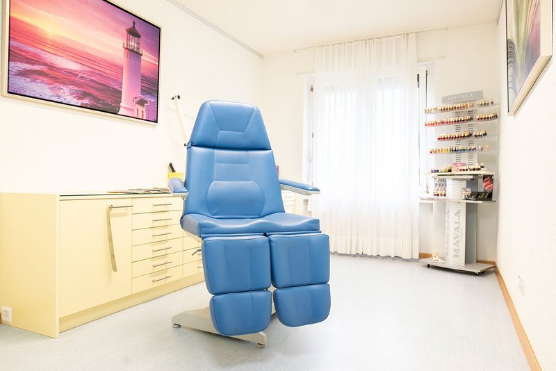 Heller Behandlungsraum der Podologie Gümligen mit blauem Behandlungsstuhl, Arbeitsschrank und Tageslicht am Fenster
